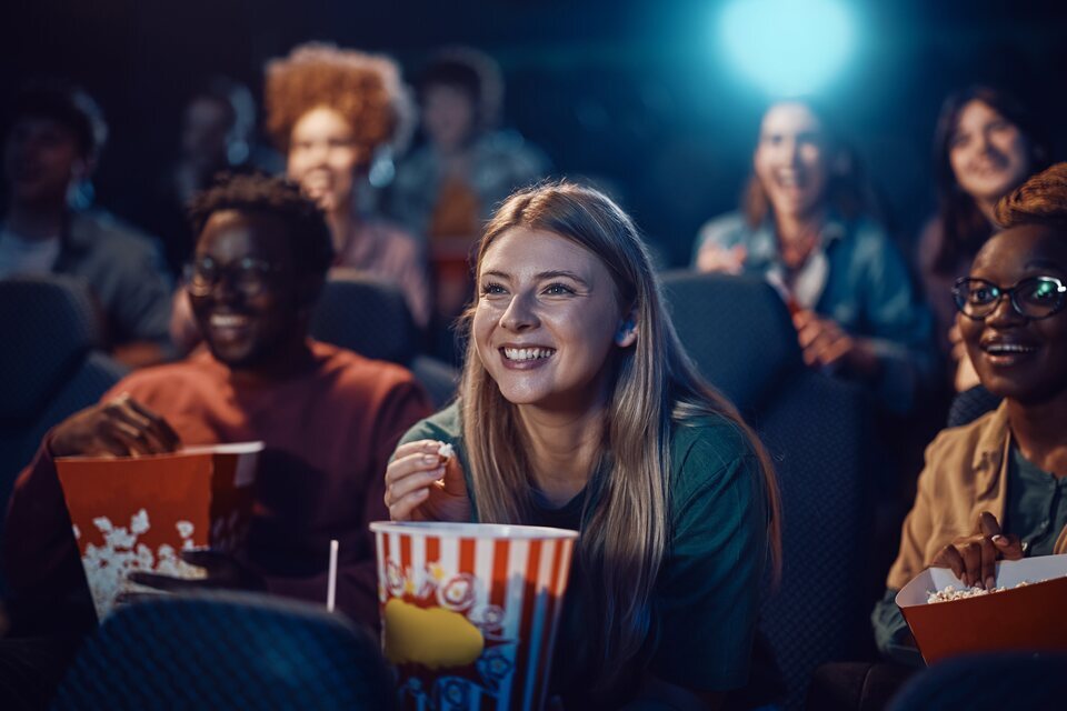 Mujer feliz comiendo palomitas durante el estreno de la película en un cine.